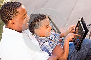 African American Father and Mixed Race Son Using Computer Tablet on Bench in Park