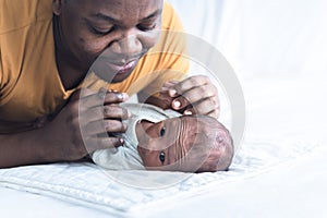 An African American father is playing tease with his 12-day-old baby newborn son lying in bed