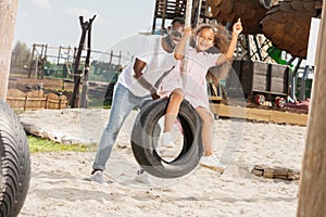 african american father pushing daughter on tire swing photo