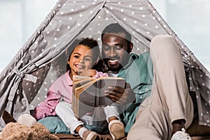 african american father reading book with child and smiling in