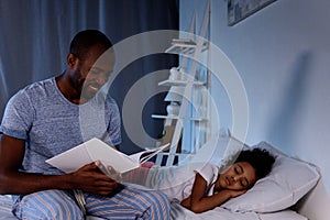 african american father reading book for sleeping daughter