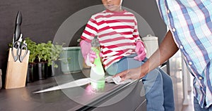 African american father and son cleaning countertop and doing high five in kitchen, slow motion