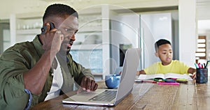 African american father and son doing homework talking on smartphone and using a laptop together