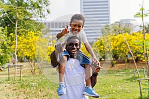 African American father and son piggyback in park. Fatherhood and happy family lifestyle concept