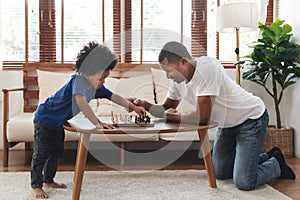 African American Father and son playing chess in living room together. Happy Black Family engaged in board game on holiday