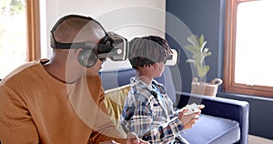 African american father and son playing video game using vr headsets at home, slow motion