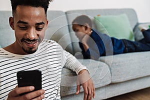 African american father and son using mobile phone while resting