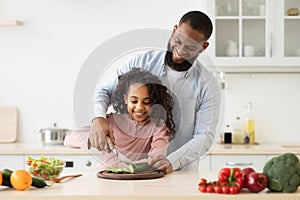 African american father teaching daughter how to prepare salad