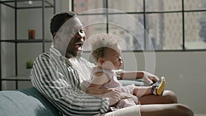 African American father with toddler girl watches TV