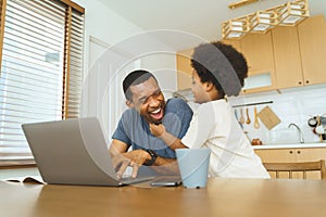 African American father working from home on laptop while his Cheerful son distracts