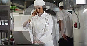 African american female chef using laptop in restaurant kitchen