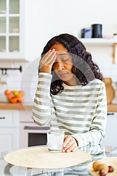 African-American female dealing with headache. Dissolving pill in glass of water