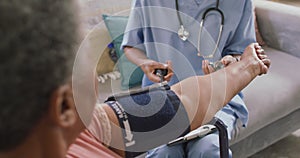 African american female doctor checking blood pressure of african american senior woman at home