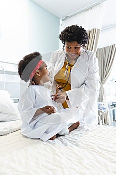 African american female doctor examining girl patient using stethoscope at hospital