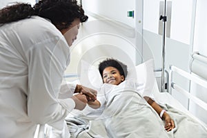 African american female doctor talking to girl patient lying on bed in corridor at hospital