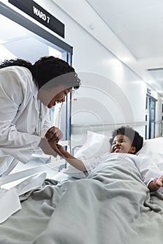 African american female doctor talking to girl patient lying on bed in corridor at hospital