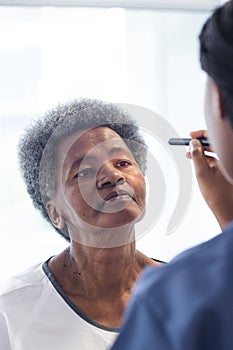 African american female doctor testing eyes of senior female patient in hospital room