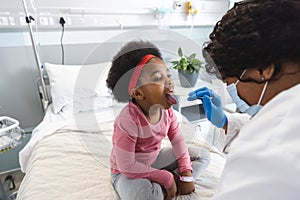 African american female doctor wearing face mask examining girl patient at hospital