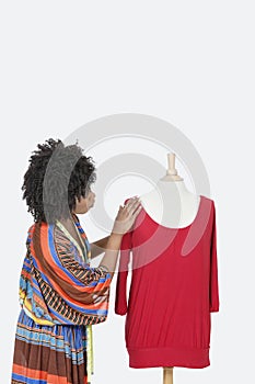 African American female fashion designer looking at red tunic over gray background