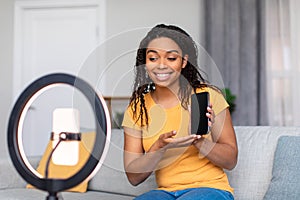 African american female influencer filming video review of modern smartphone on phone webcamera at home