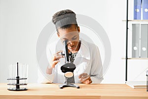 african american female lab technician looking through microscope in lab.