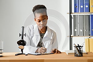 african american female lab technician looking through microscope in lab.
