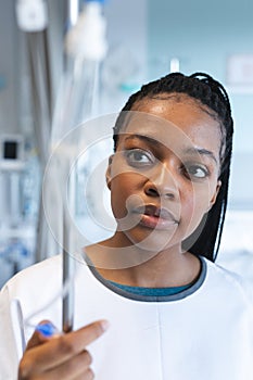 African american female patient wearing hospital gown, holding drip in hospital room