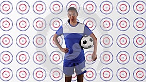 African american female soccer player holding a ball against stars on multiple spinning circles