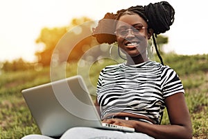 African american female student sitting in park working on laptop preparing for exams outdoors