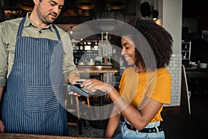 African American female tapping credit card making payment for coffee sitting in trendy cafe.