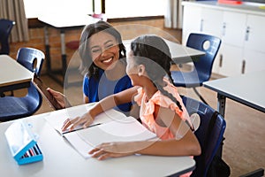 African american female teacher with digital tablet teaching a girl at elementary school