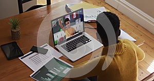 African american female teacher talking and taking notes while having a video call on laptop at home