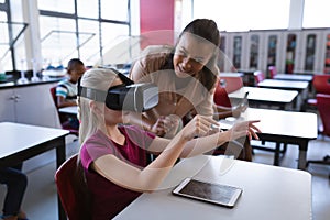 African american female teacher teaching caucasian girl to use vr headset in the class at school