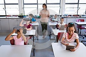 African american female teacher teaching students to use electronic devices in the class at school