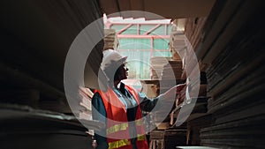 African American female worker inspects stock order at paper factory warehouse.