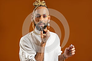 African american gay applying make up isolated on brown background