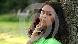 African American girl biracial teenager young woman outside sitting leaning against a tree thinking