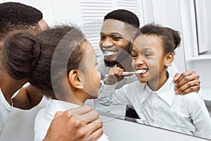 African-american girl brushing teeth together with dad