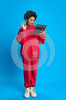 African-American girl in casual clothes using tablet for online video call, communication against blue studio background