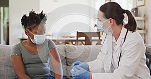 African american girl and caucasian female doctor wearing face masks, vaccinating