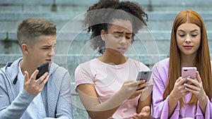 African-american girl displeased with bad photo comment showing phone to friends