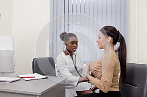 An African-American girl Doctor listens, examines a patient with a stethoscope in her office at the hospital.