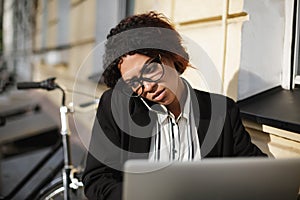 African American girl in glasses sitting at the table of cafe and working on her laptop. Lady with dark curly hair in