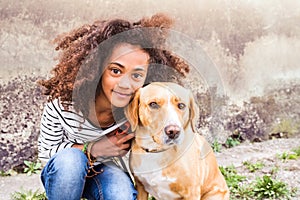 African american girl with her dog against concrete wall.