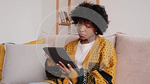 African american girl holding digital tablet touch screen typing scroll page at home. Woman with mobile tech device