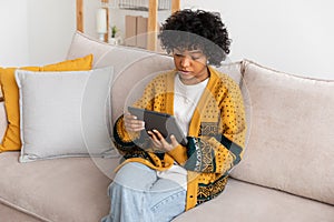 African american girl holding digital tablet touch screen typing scroll page at home. Woman with mobile tech device