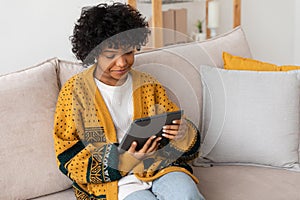 African american girl holding digital tablet touch screen typing scroll page at home. Woman with mobile tech device