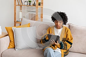 African american girl holding digital tablet touch screen typing scroll page at home. Woman with mobile tech device