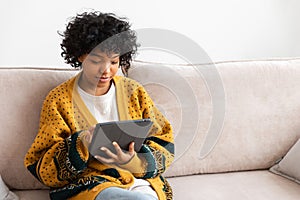 African american girl holding digital tablet touch screen typing scroll page at home. Woman with mobile tech device
