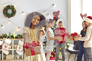 African-American girl holding out hands with Christmas present, looking at camera and smiling